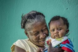 Haitian woman holding toddler in front of green backdrop.