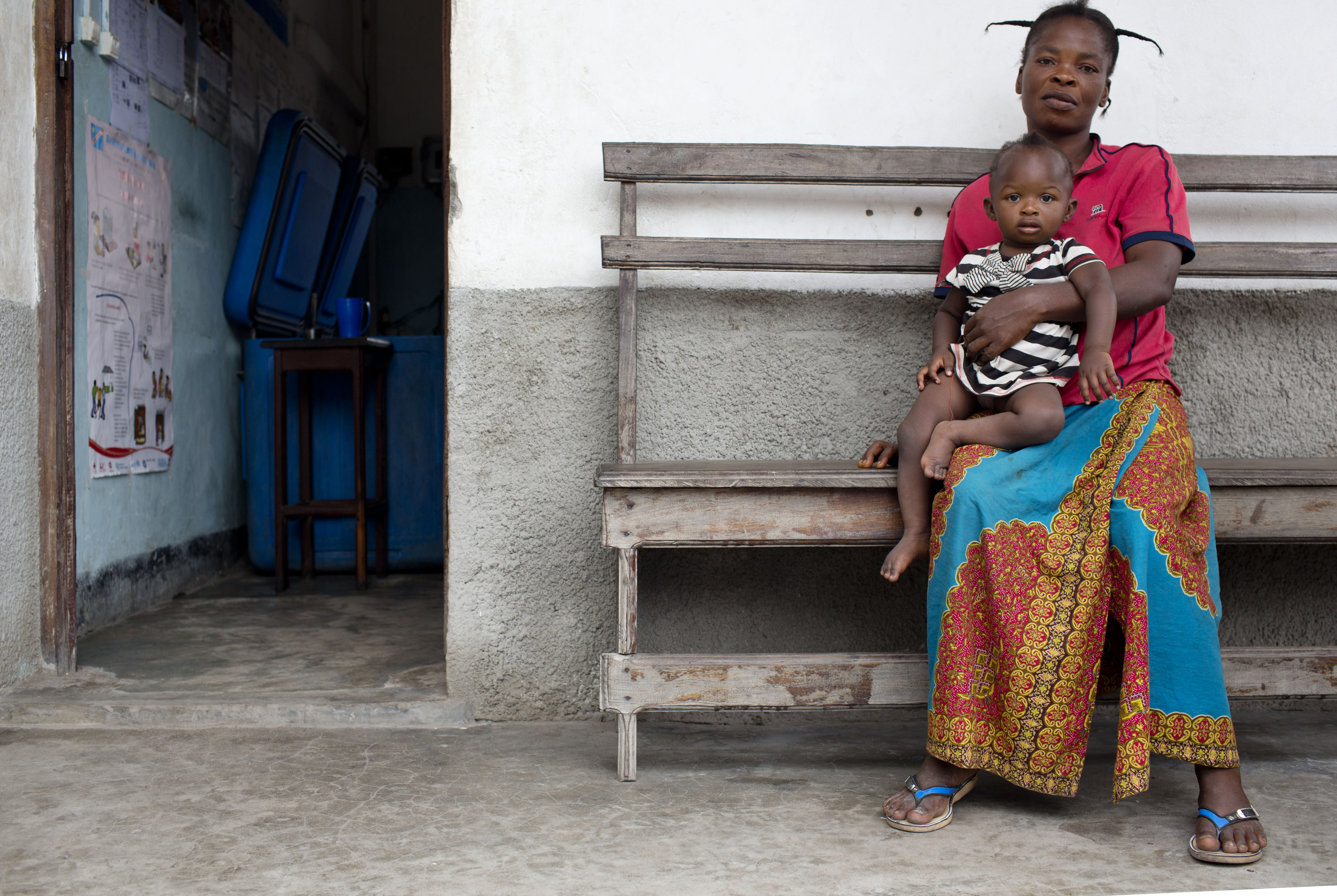 Woman holding her infant sitting on a bench in front of a building.