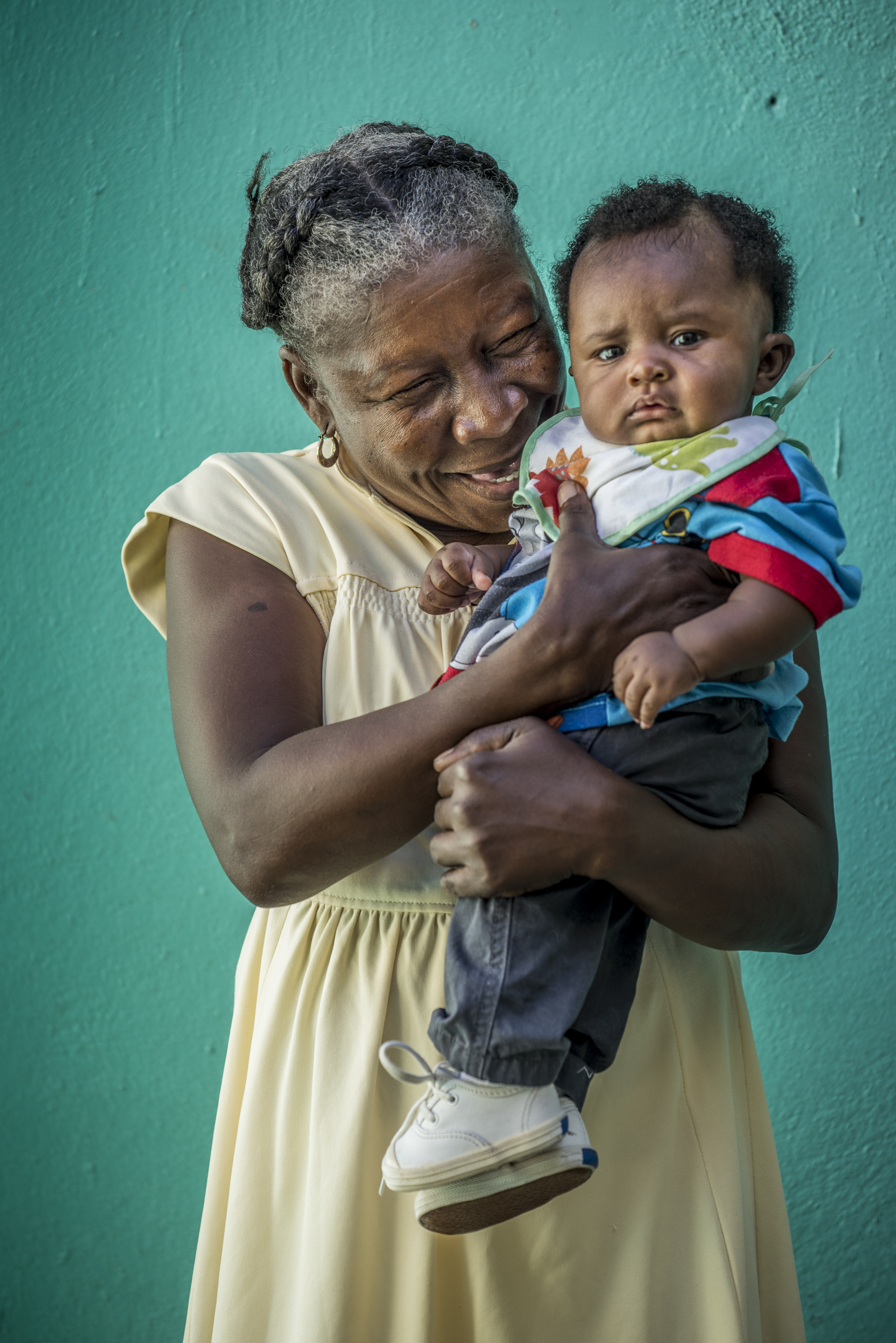 Haitian woman holding toddler in front of green backdrop.