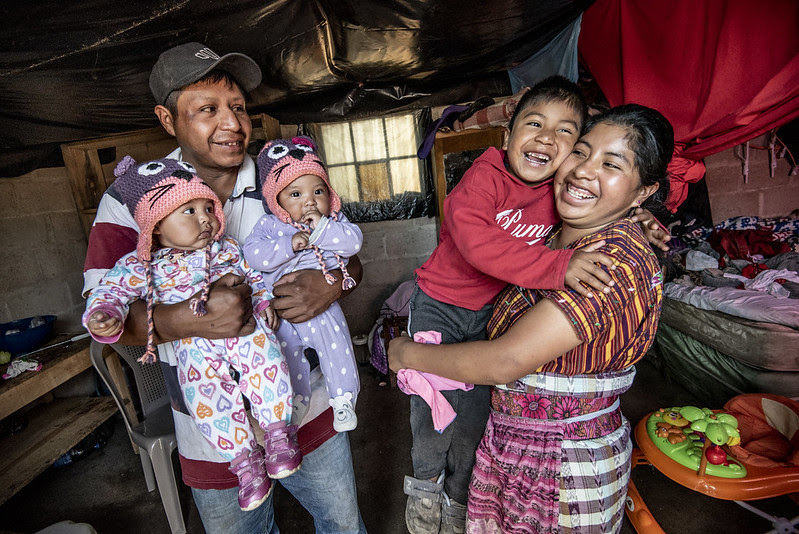 Happy family holding their three kids inside their home.