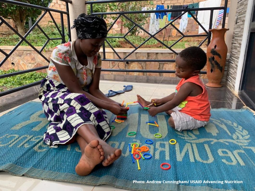 Jeune mère africaine et son enfant assis dehors sur un tapis du HCR, jouant avec des jouets de construction
