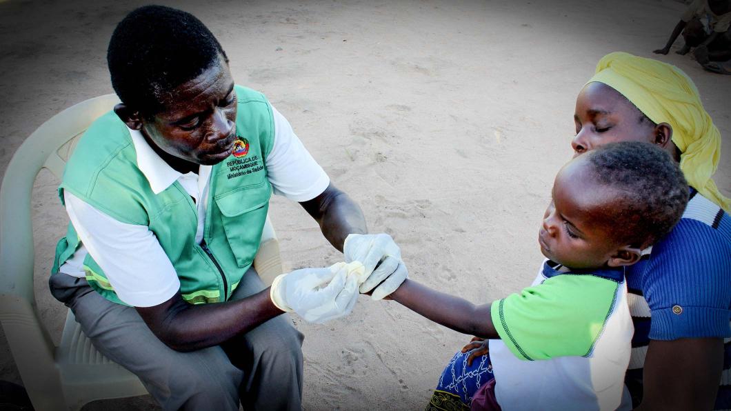 Photo d'un homme prodiguant des soins de santé à un enfant sur les genoux d'une femme.