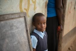 Photo of a young child standing next to a blackboard.