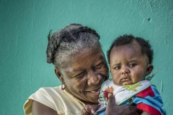 Femme haïtienne tenant un tout-petit devant un fond vert.