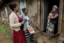 two women stand next to a woman holding an infant in a doorway