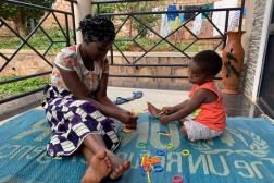 Jeune mère africaine et son enfant assis dehors sur un tapis du HCR, jouant avec des jouets de construction en plastique