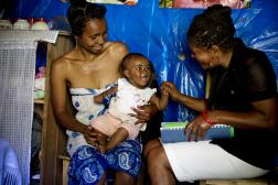 A woman holds her infant while a nurse smiles and holds her hand. 