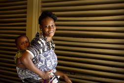 Mère africaine tenant son bébé dans un porte-bébé sur le dos, souriante